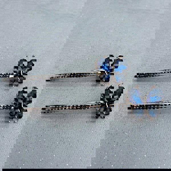 Gold hair slides, butterfly design, deep blue crystal wings, long slim barrette style, rhinestone detailing along stem, elegant decorative accessories, sparkling vintage inspired look
