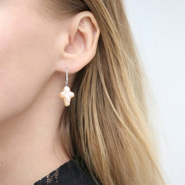 Cross-shaped pearl drop earrings crafted from sterling silver shown on a blonde model.