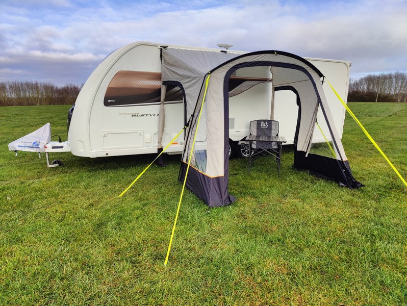 An image of the View Lite 260 Caravan Awning from OLPRO in a field attached to a caravan with some camping furniture inside.