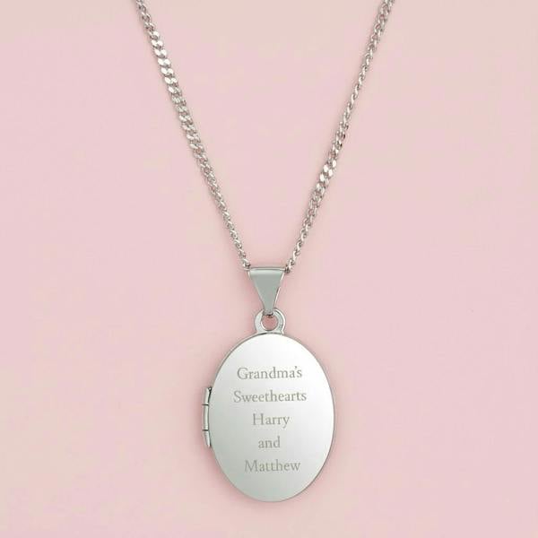 Close-up of the back of a polished sterling silver oval locket necklace, showing the custom engraved message 'To Mummy With Love & Kisses From Ida x' on a pink background.