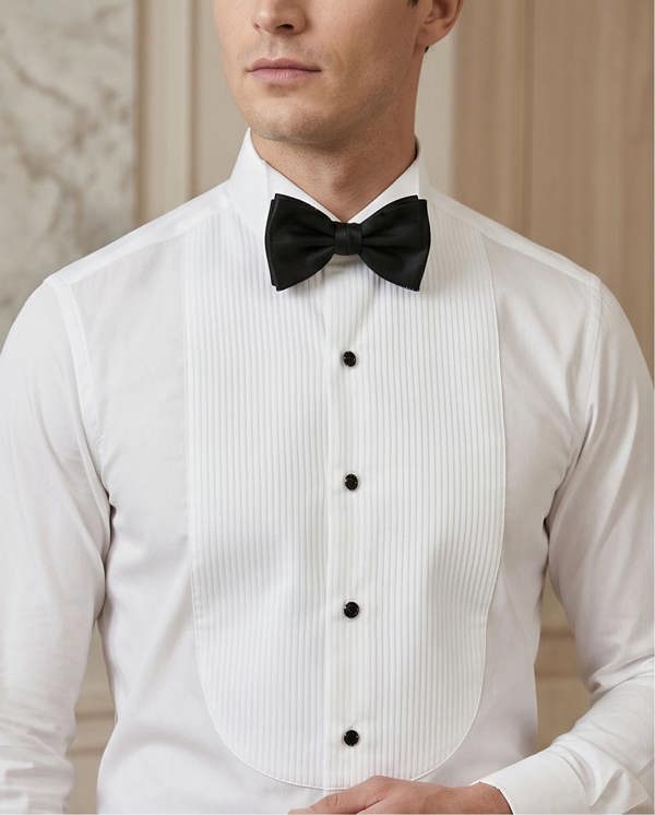 A man wearing a white pinstriped formal tuxedo vest with black buttons, a white dress shirt, and a black bow tie, shown from the chin down against a soft beige background.