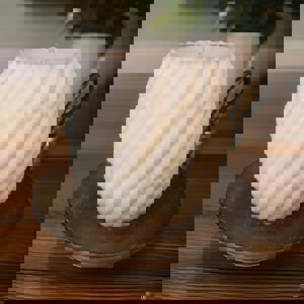 Two white unscented natural wax pillar candles, one lit, providing a soft glow, on a dark background.