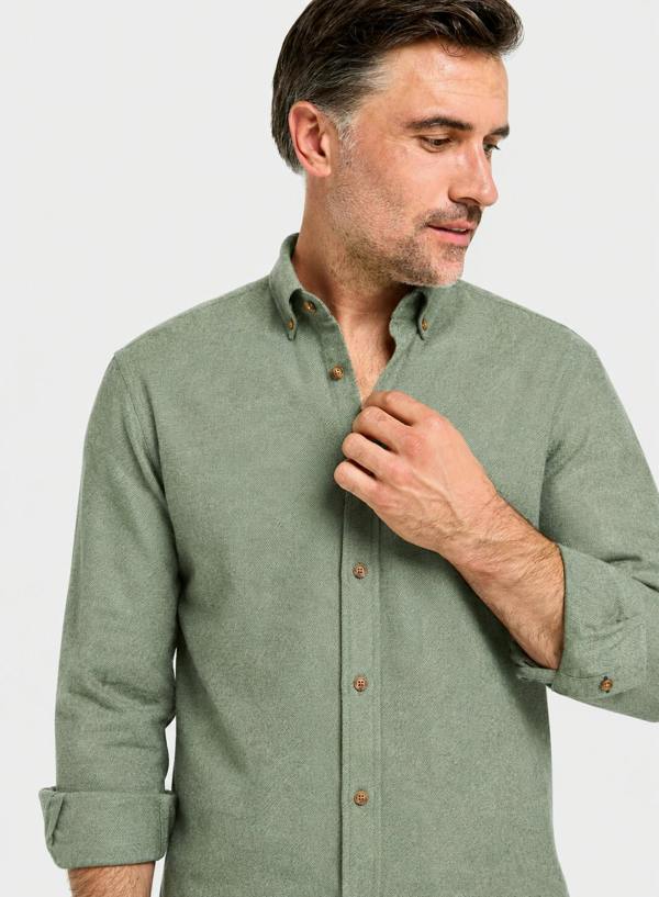 A man wearing a sage green long-sleeve button-down shirt, shown from the chest up against a light gray studio background.