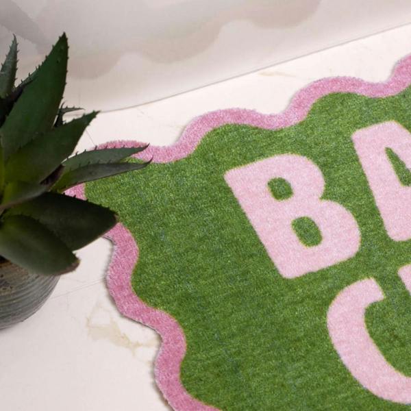 Green and pink bath mat with 'Bath' text on a marble surface next to a plant.