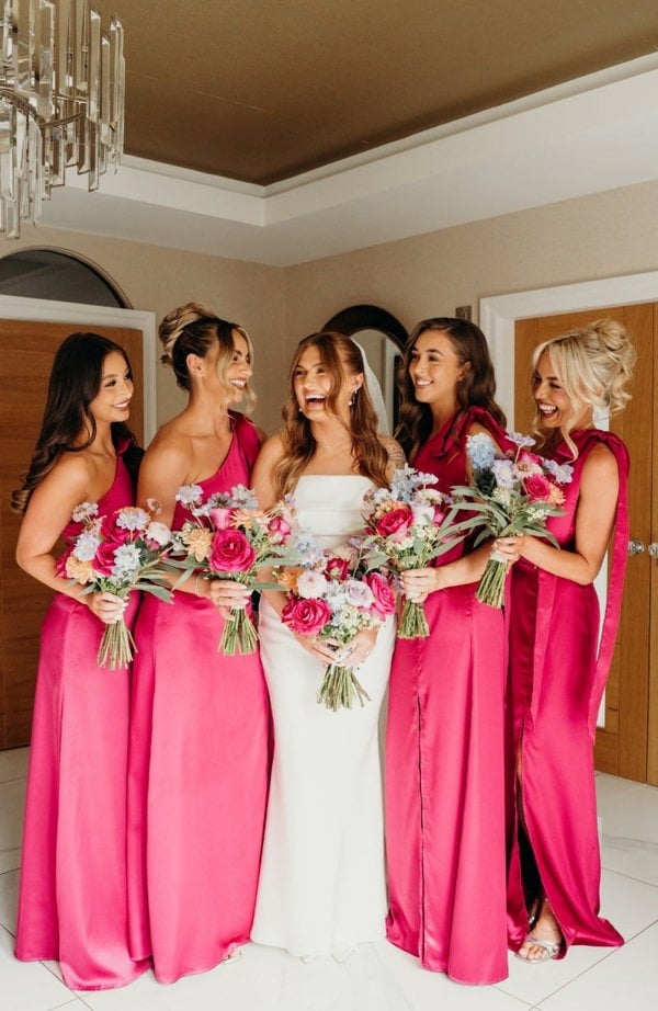 Bride with four bridesmaids in pink dresses holding bouquets indoors.