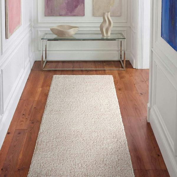 Beige runner rug on a wooden floor with a glass table and decorative items in the background.