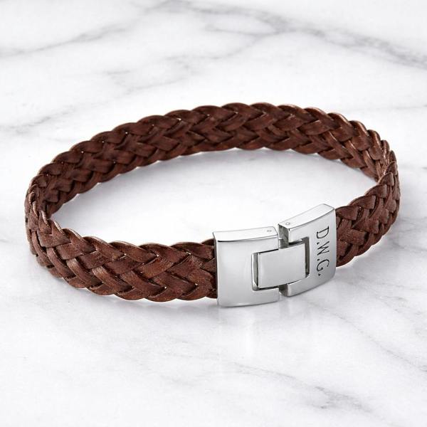 Personalised soft brown woven leather bracelet with a hard-wearing stainless steel clasp engraved with initials D.W.G. on a marble surface.