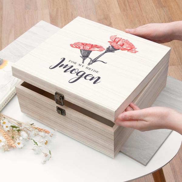 A close-up of hands opening a personalised light wood pine box printed with pink carnations and "For My Bride Imogen".