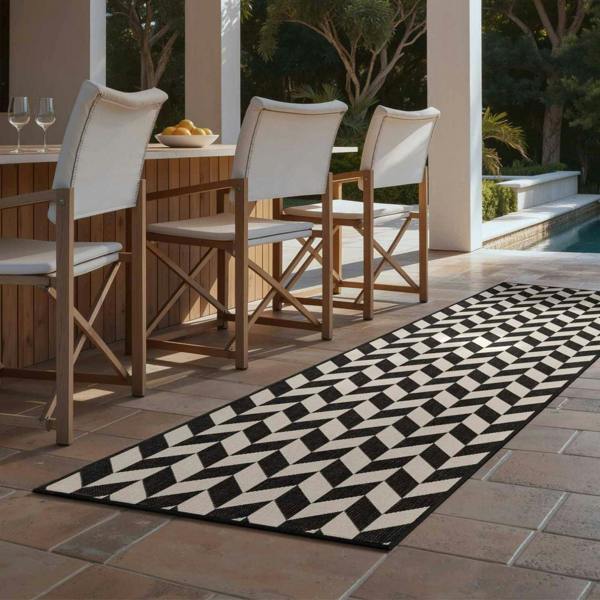 Outdoor dining area with wooden chairs and a black and white patterned rug.
