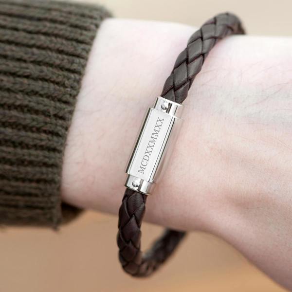 A close-up lifestyle shot of the Personalised Men's Roman Numerals Woven Leather Bracelet in brown being worn on a man's wrist, styled next to the cuff of a ribbed khaki green jumper.