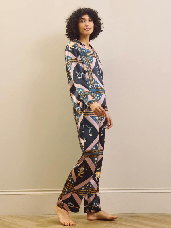 Woman wearing a celestial patterned satin pyjamas standing against a plain wall.