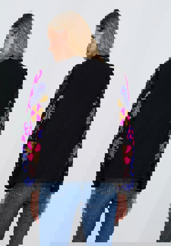 Person wearing a black jacket with colorful floral patterns on sleeves against a white background