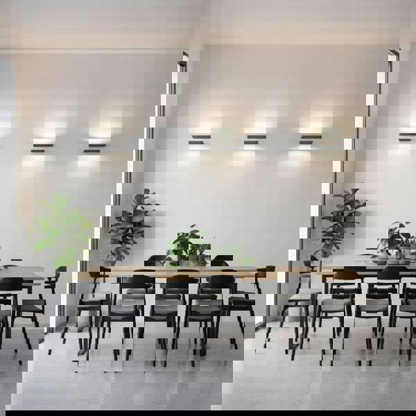 Black internal wall uplighters o a grey wall with a table and chairs and plants in the room