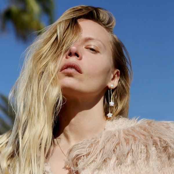 Lena Wro wearing gold starry earrings. Blue sky background.