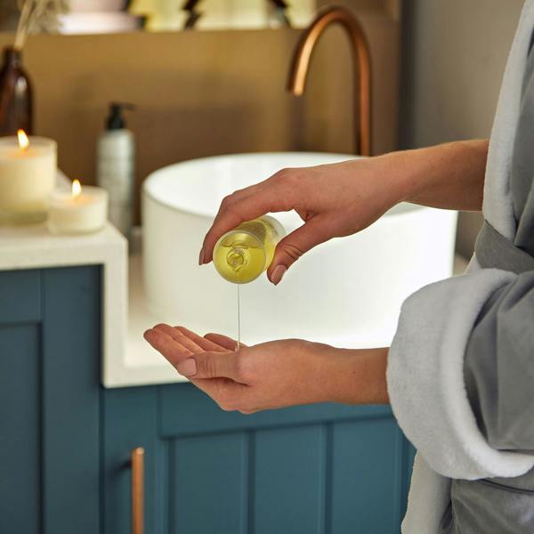 Person wearing a Scentered bathrobe pouring Scentered Sleep Well body oil into their hand