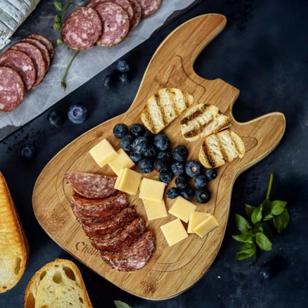 An acoustic guitar-shaped bamboo cutting board laid out as a charcuterie serving platter with cheeses, meats, crackers, and grapes.