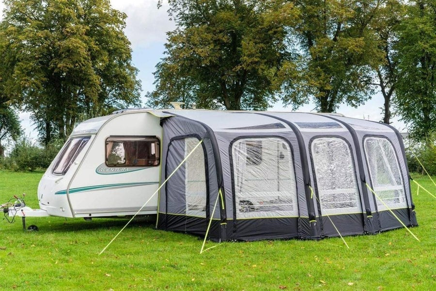 The OLPRO View 420 Caravan Inflatable Porch Awning With Porch Extension attached to a caravan at a campsite with a treeline in the background.