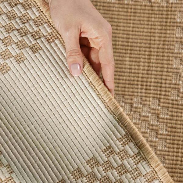 Close-up of a hand touching a textured beige and brown rug.
