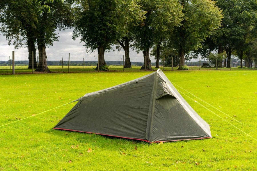 The OLPRO Hawford Lightweight 2 Person Tent pitched in a field with a treeline in the background, the doors are closed and the vents are open.