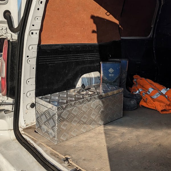 Aluminium tool box 35L in a vehicle's cargo area, featuring a diamond plate texture and a shiny silver finish, with orange work gear nearby