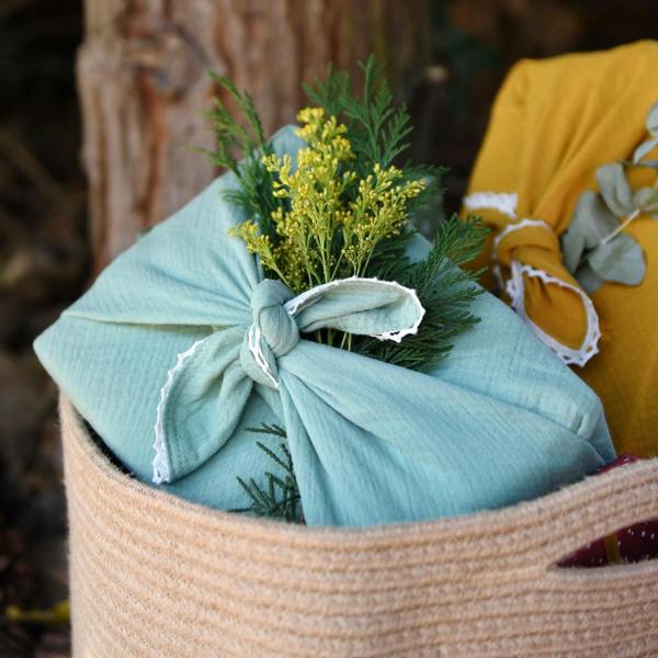 Reusable mint green fabric gift wrap with lace trim tied in a knot around a present