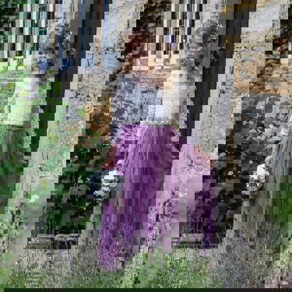 A young girl wearing a heather-colored, long sleeve, floral girls' dress with a straight layered tulle skirt standing outdoors.