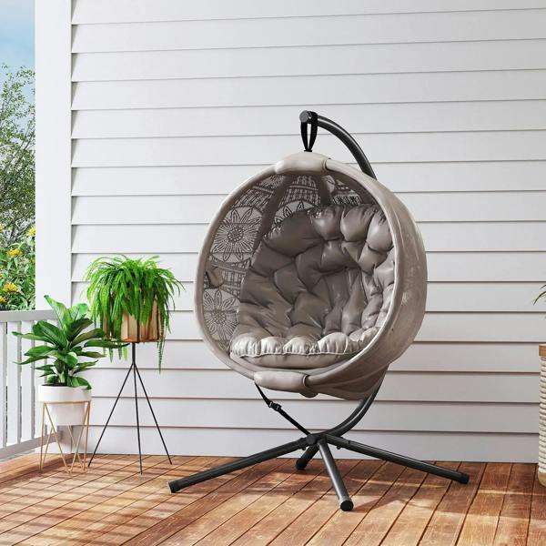 Round egg basket chair with gray cushion and black steel stand beside outdoor plants