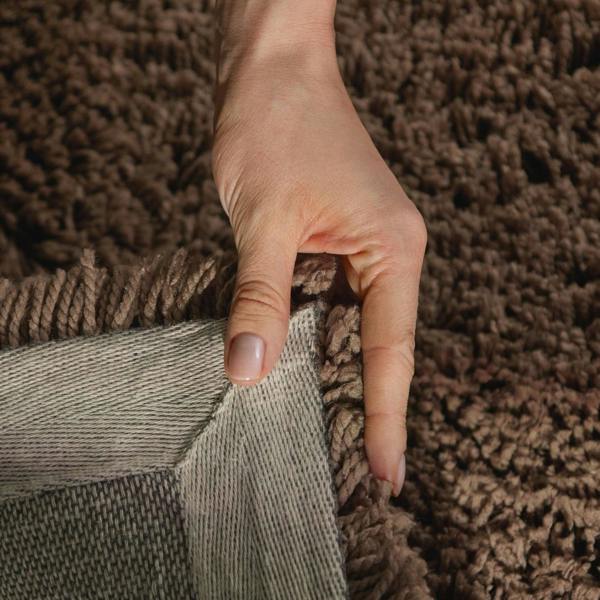 Hand holding a corner of a textured brown rug
