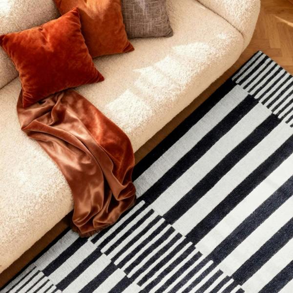 Beige sofa with orange cushions and a brown blanket next to a black and white striped rug.