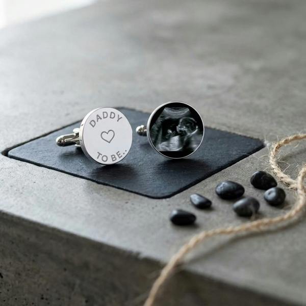 Abode Home & Gifts 'Daddy To Be' personalised baby scan cufflinks displayed on a dark slate coaster over a modern concrete counter.