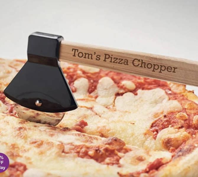 A close-up of the Personalised Axe Shaped Pizza Cutter rolling through a fresh cheese and tomato pizza, with 'Tom's Pizza Chopper' engraved on the wooden handle.