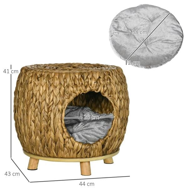 Wicker cat bed house with grey cushion insert and round doorway, with wooden legs