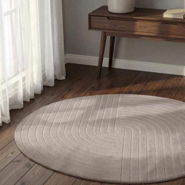 Round gray rug on a wooden floor with a wooden side table and white curtains.