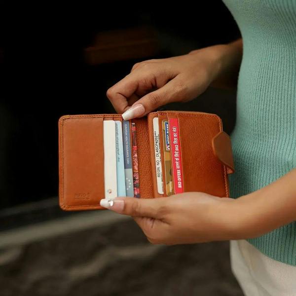 Person holding a cognac wallet with cards inside, wearing a green sweater.
