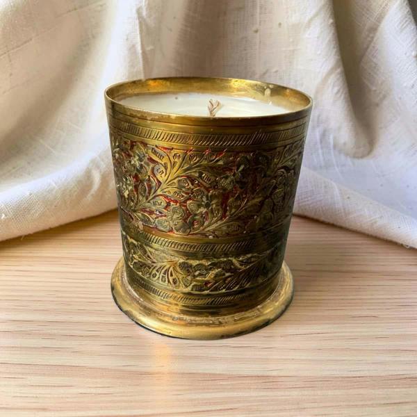 Decorative candle in an ornate brass holder on a wooden surface with a white fabric background