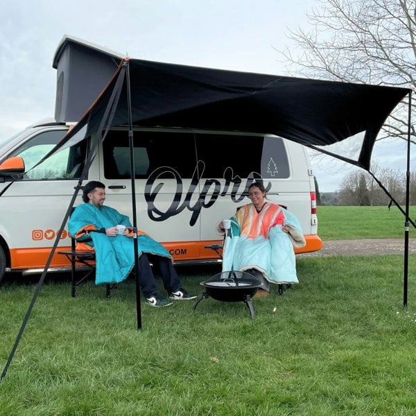 A male and female sat under the Modern Shade Canopy from OLPRO that is attached to Volkswagen Campervan.