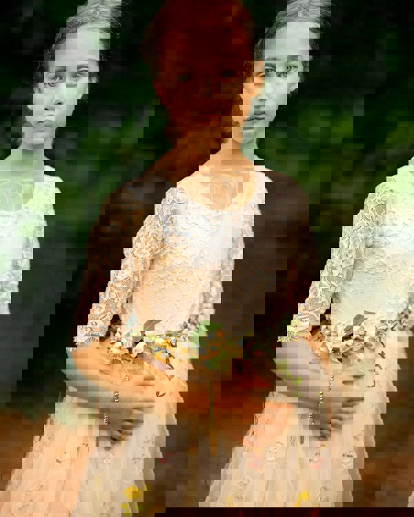 Young girl in a floral dress holding flowers against a blurred natural background