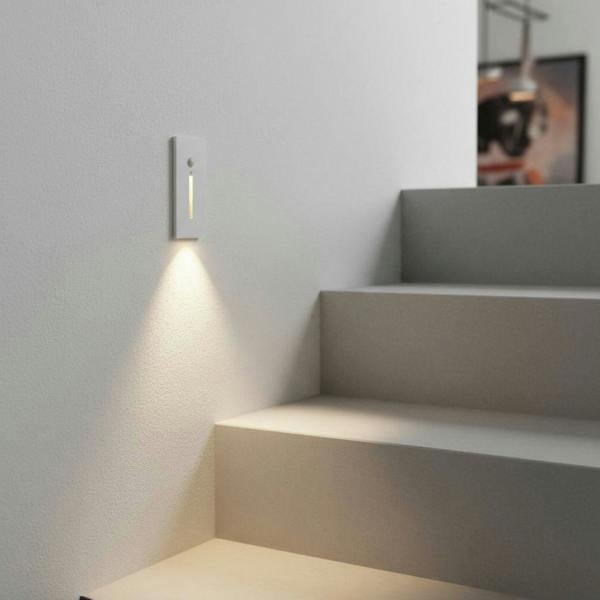 white motion sensor step light installed on a white wall next to some white stairs 