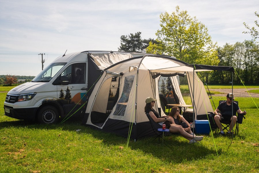 A group of people relaxing outside of the Cubo XL Motorhome Awning - Fibreglass Poles that is attached to a Crafter.