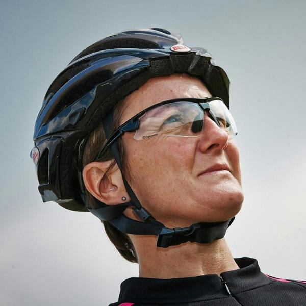 Cyclist in black helmet wearing Optimum sunglasses with clear lenses against grey sky, lifestyle shot - Optimum
