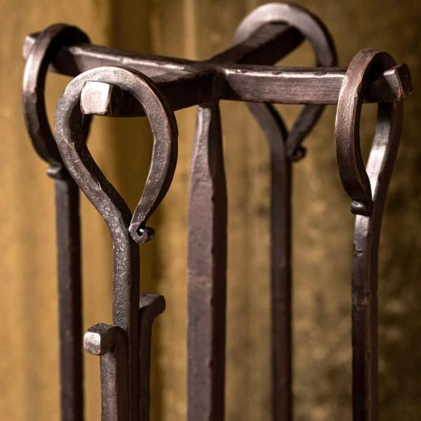 Close-up detail of the loop handles and central stand on the antiqued brown wrought iron fireside companion set.