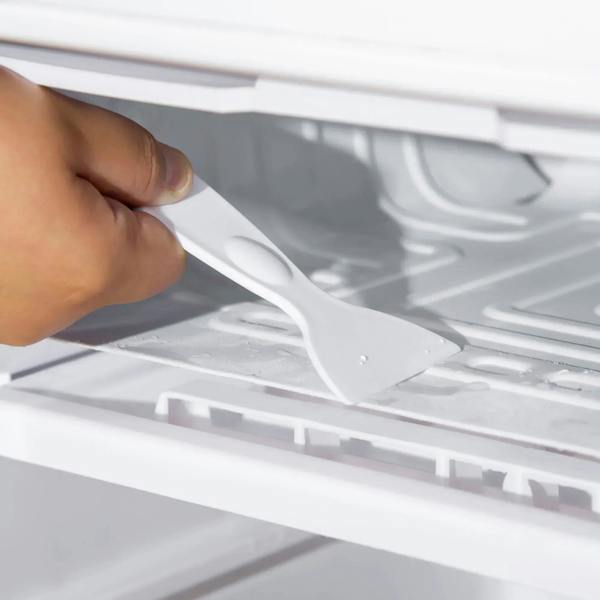 Hand lifting a white fridge interior shelf with removable tray rails inside the mini fridge.