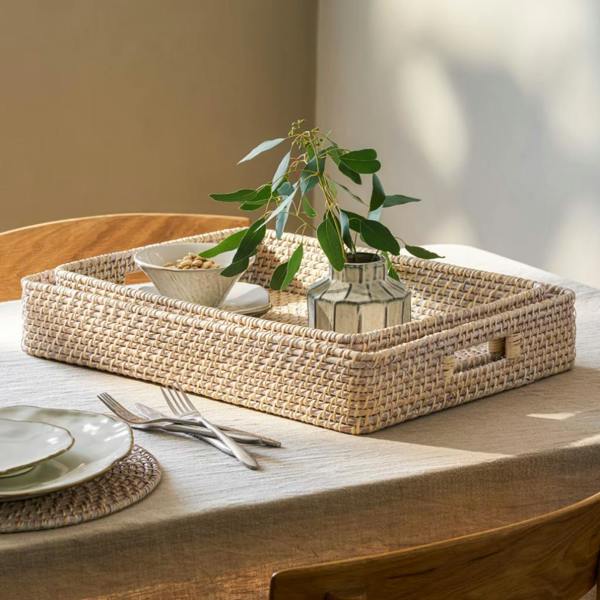 Set of two nesting rectangular whitewash rattan trays styled on a dining table with a vase.