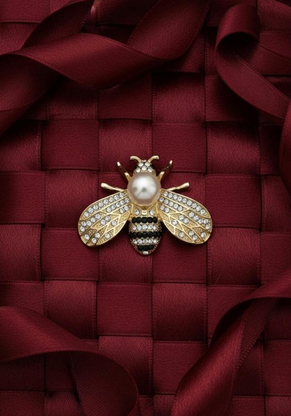 Gold bee-shaped brooch with a pearl on a red textured fabric background