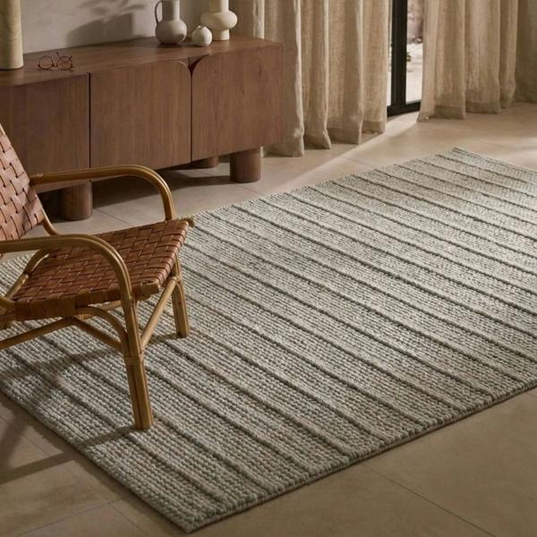 Striped rug on a floor with a wooden chair and sideboard in the background.