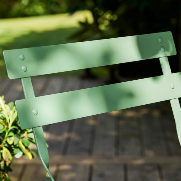 Close-up shot showing the smooth slatted backrest and rivet details of a thistle green metal folding bistro chair.