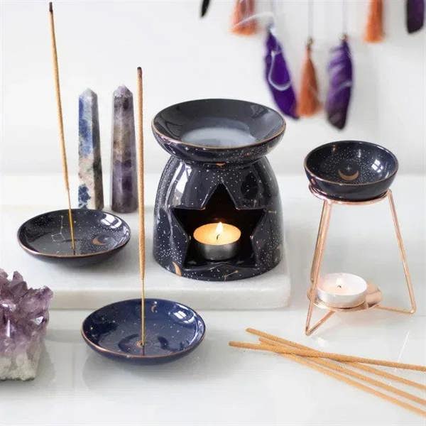 Constellation oil burner with star cut-outs, black ceramic, gold rim and lit wax candle