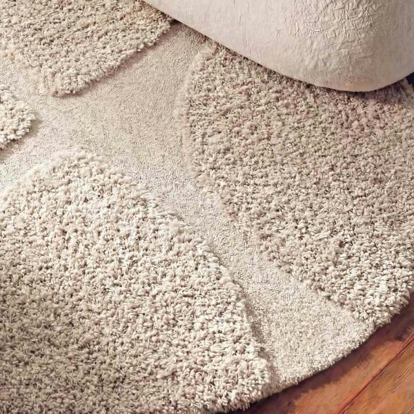 Close-up of a beige carpet being rolled out on a wooden floor