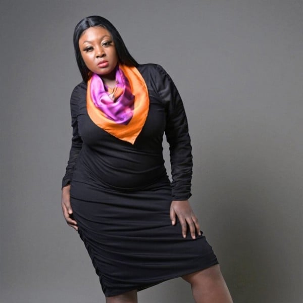 Plus-size woman wearing a black Boudicca Ruched Bodycon Midi Dress, styled with our Pink Purple Silk Scarf. Plain Background.