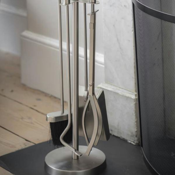 A premium four-piece silver fireside tool set standing next to a marble fireplace hearth and black mesh fire screen.